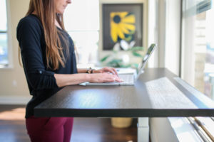 woman at a standing desk typing on her laptop