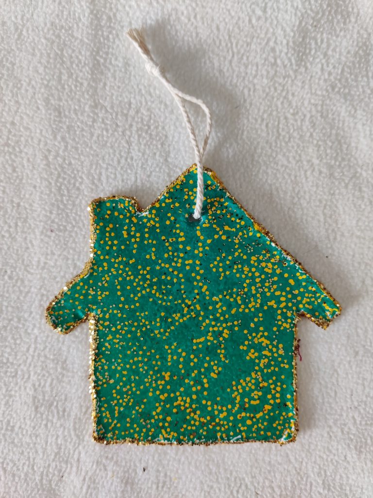 image shows a tiny home made from clay and decorated with green and yellow paint with gold glitter stuck around the outline
