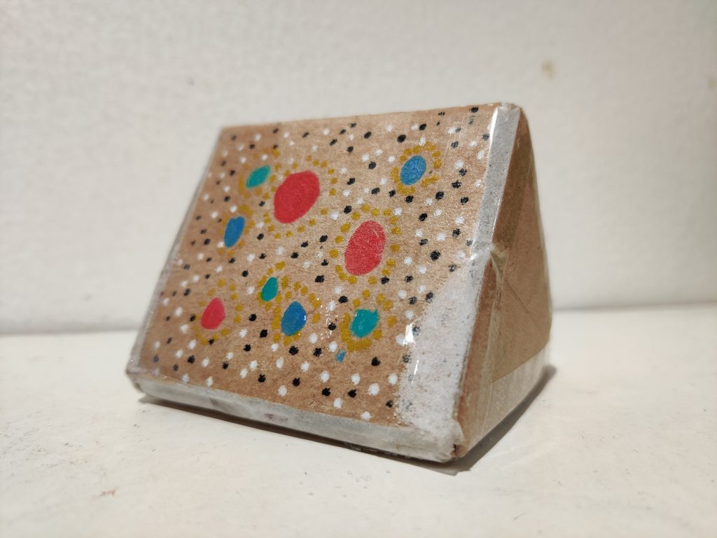 A 3D rattle made from cardboard and sellotape with colourful circles and dots painted on the triangular shape