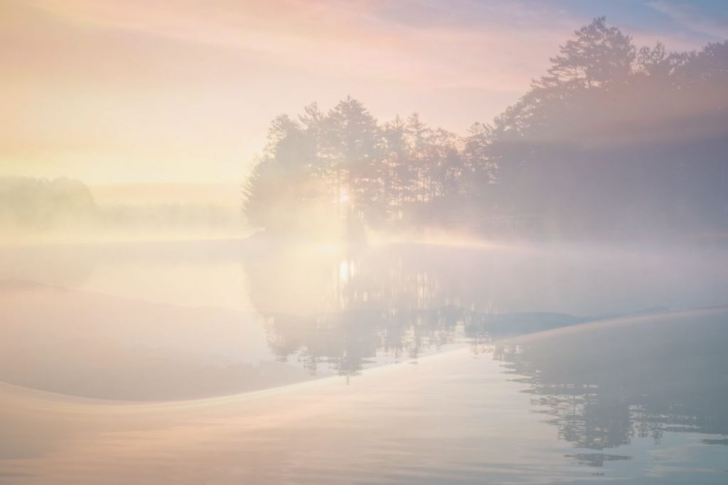 Soft mist over a lake at sunrise, with trees surrounding, merged with gentle pastel colours, wide open sky, calm and spacious feeling, minimal, atmospheric