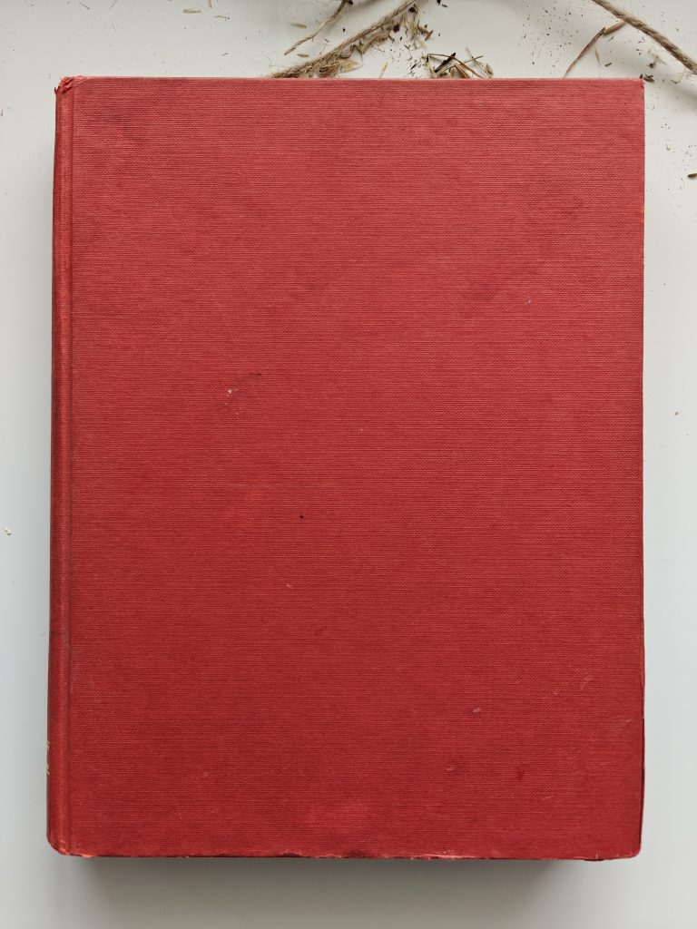 red hardback book on white table with grass seeds nearby