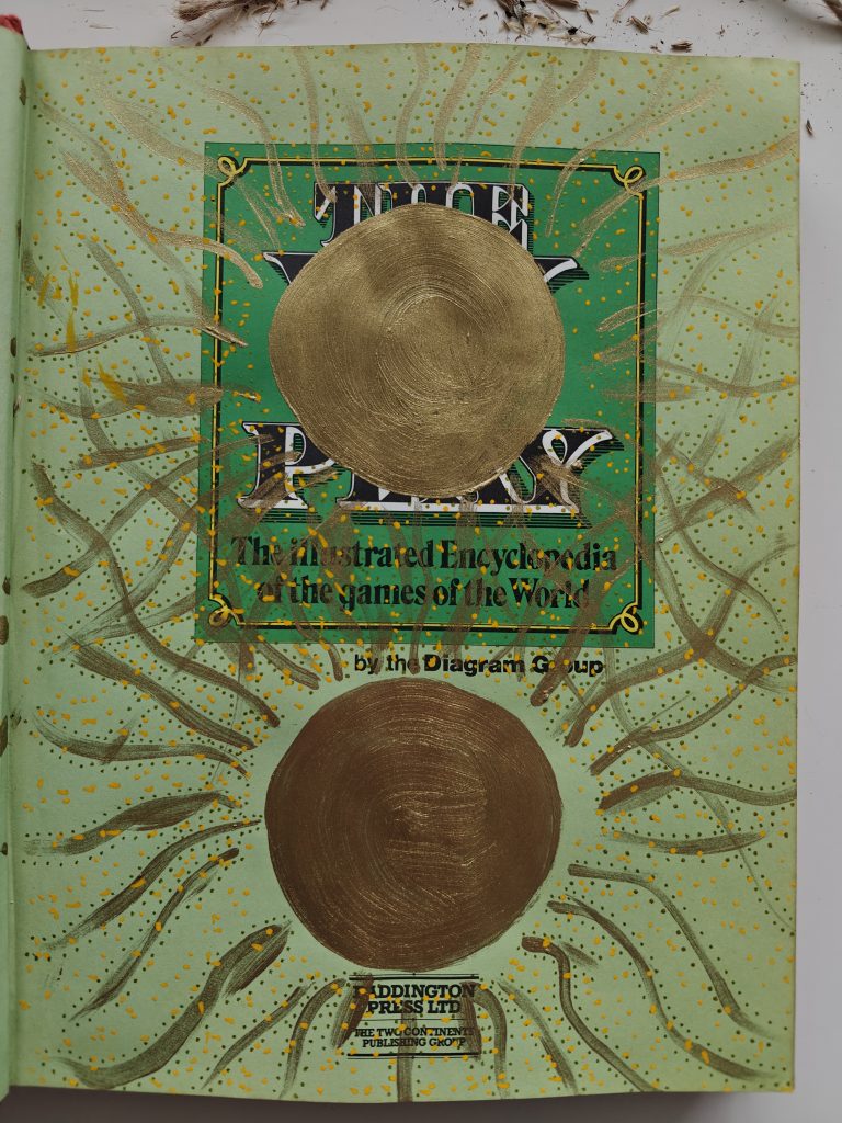 Two suns in gold paint covering printed matter on a green page of a book