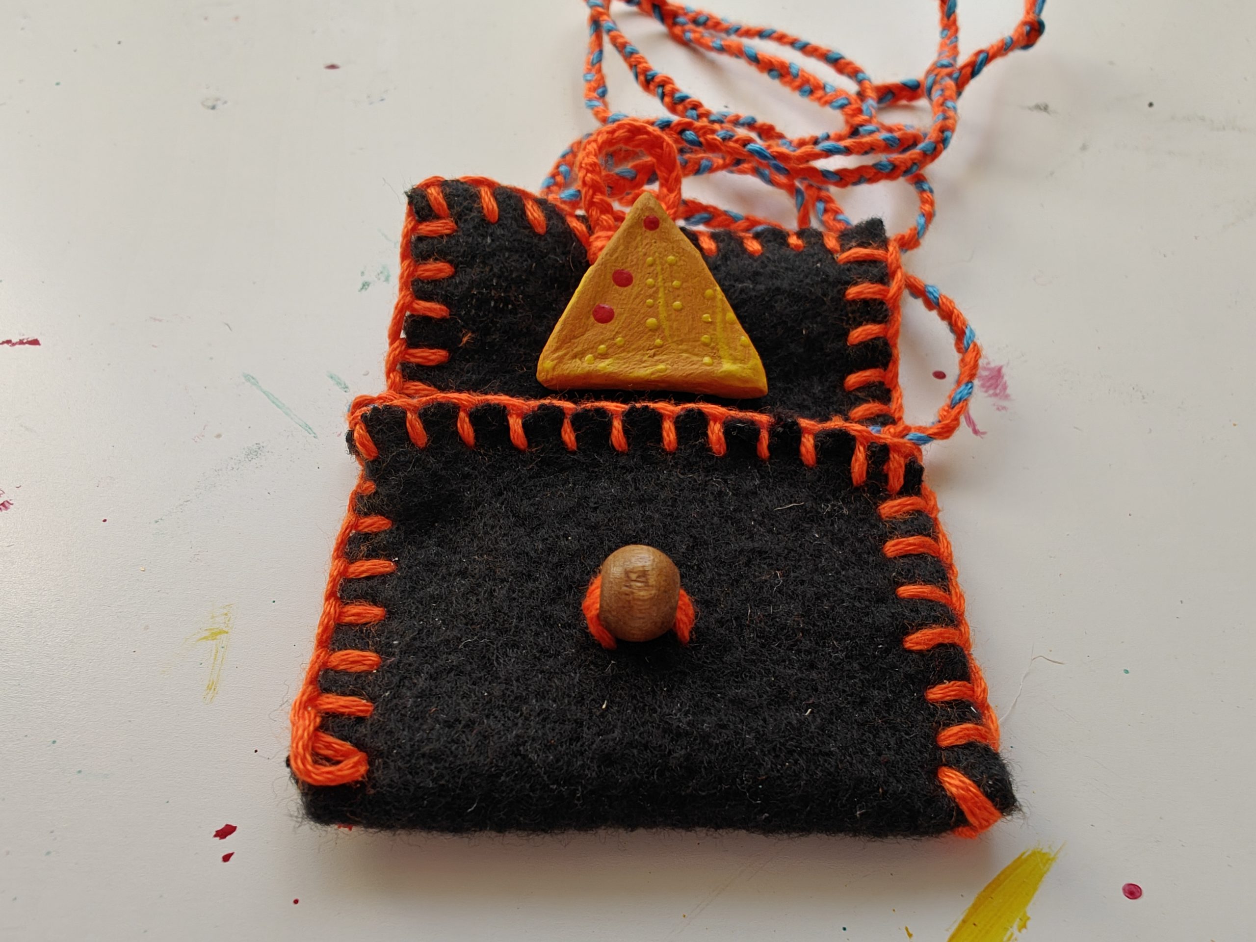 a black fleece pouch sewn with orange stitching and a triangular talisman rests on the pouch lid